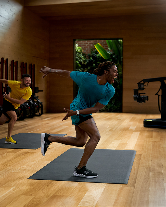 비디오 스튜디오에서 카메라 앞에 서서 세션을 진행하고 있는 Apple Fitness+ 트레이너들. 