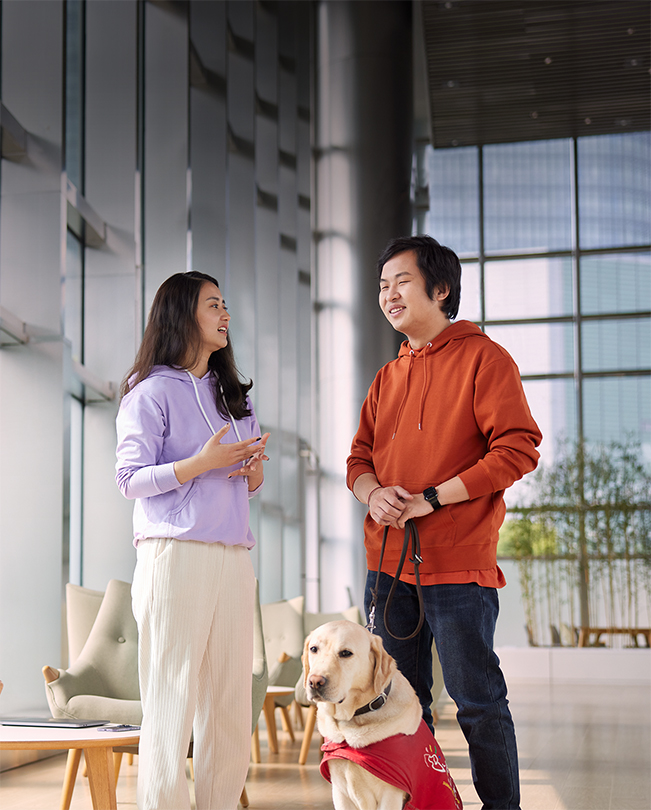 Dois funcionários da Apple a conversar numa área comum luminosa, um deles segura a trela de um cão de serviço.