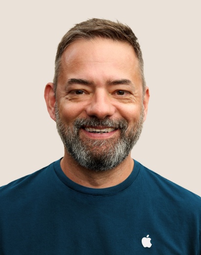 Un dipendente Apple Retail sorridente con i capelli corti grigi e la barba.