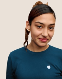 Una dipendente Apple Retail sorridente con i capelli lunghi scuri e riflessi rosa.