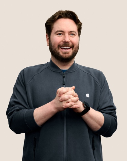 Un dipendente Apple Retail sorridente con i capelli corti, mossi e scuri e la barba.