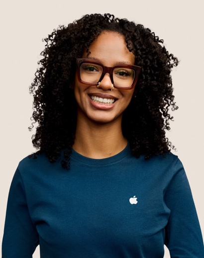 Una dipendente Apple Retail sorridente con i capelli lunghi, ricci e scuri, e gli occhiali da vista.