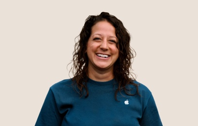 Una dipendente Apple Retail sorridente con i capelli lunghi, mossi e scuri.