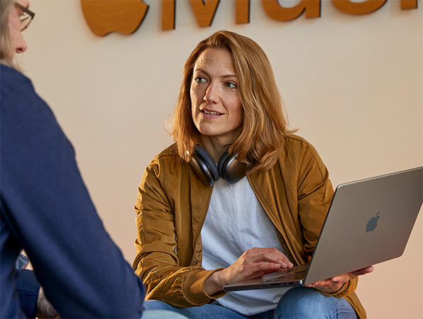 会話している2人のセールス＆ビジネスディベロップメント関連職のAppleチームメンバー。一人はMacBookを手に持ち、Apple Musicのロゴがある壁の前に座っている。