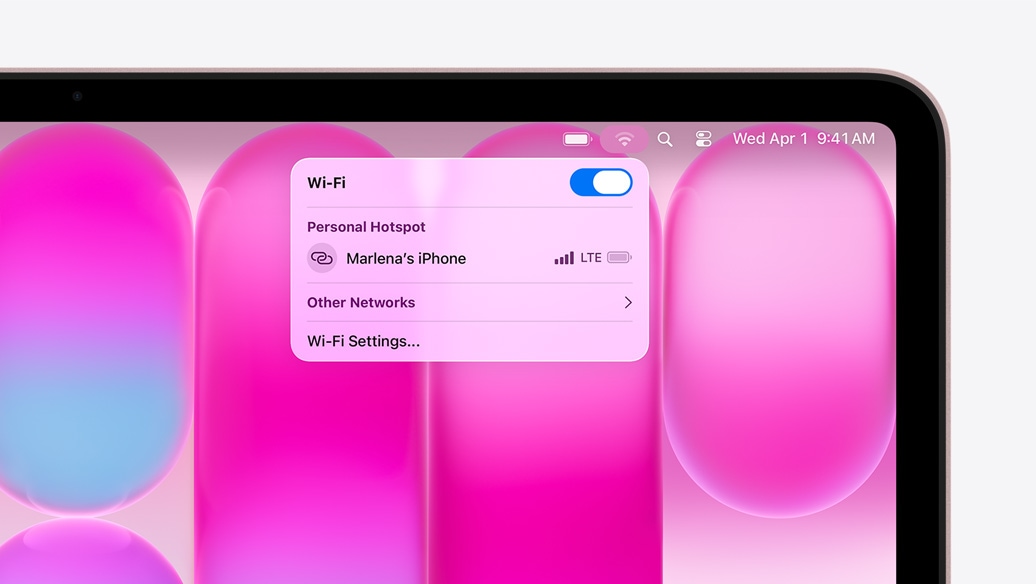 MacBook Neo w kolorze subtelnego różu, w menu Wi-Fi widać sekcję Hotspot osobisty z opcją wyboru „iPhone Marleny”
