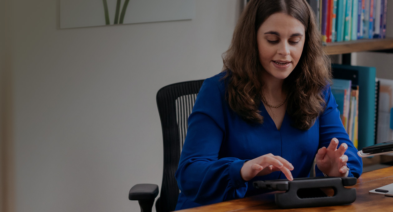 Fotó az Apple Distinguished Educator és fogyatékossági aktivista Jordyn Zimmermanről, ahogyan egy asztalnál ül és egy iPad kijelzőjén gépel