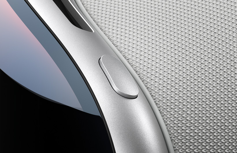 Vue en gros plan du coin supérieur gauche incurvé de l’Apple Vision Pro. Le bouton supérieur présente la même finition en aluminium que le cadre de l’appareil. Le verre incurvé à l’avant ainsi qu’une partie de l’orifice d’aération supérieur sont également visibles