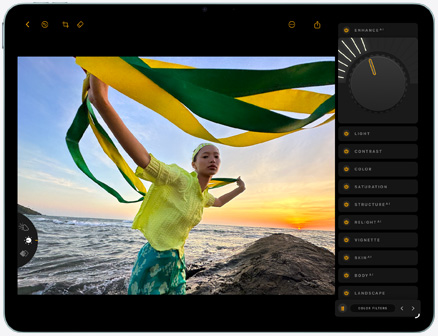 iPad Air, pohled zepředu, upravování fotky osoby držící zeleno-žlutou látku na pozadí slunce zapadajícího nad pláží, napravo jsou otevřené editační nástroje