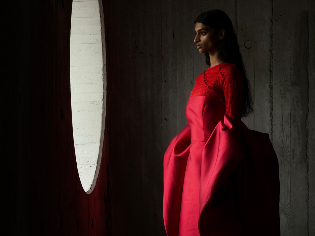 Une femme vêtue d’une longue robe rouge se fait photographier dans une pièce vide. L’app Appareil photo change de distance focale pour illustrer les capacités du système caméra pro, mettant en valeur : 200 mm