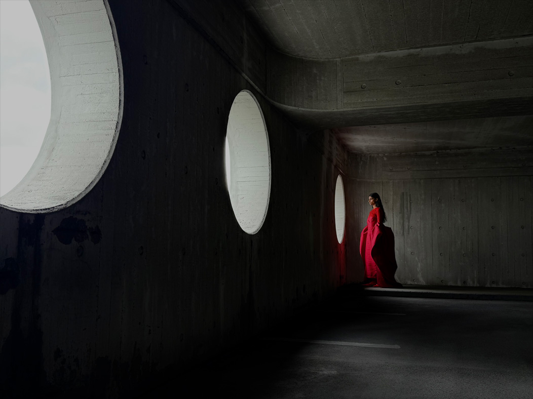 Une femme vêtue d’une longue robe rouge se fait photographier dans une pièce vide. L’app Appareil photo change de distance focale pour illustrer les capacités du système caméra pro, mettant en valeur : 35 mm