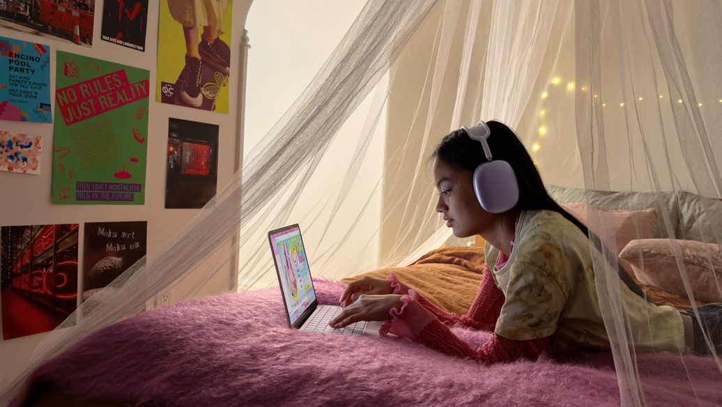 Eine junge Person in einem Schlafzimmer mit Kopfhörern nutzt ein MacBook Neo in Rosa, um einen Termin bei einem Nagelstudio zu buchen